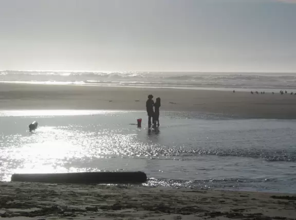 A girl and boy play in the lagoon, while the sun shimmers on the water. 