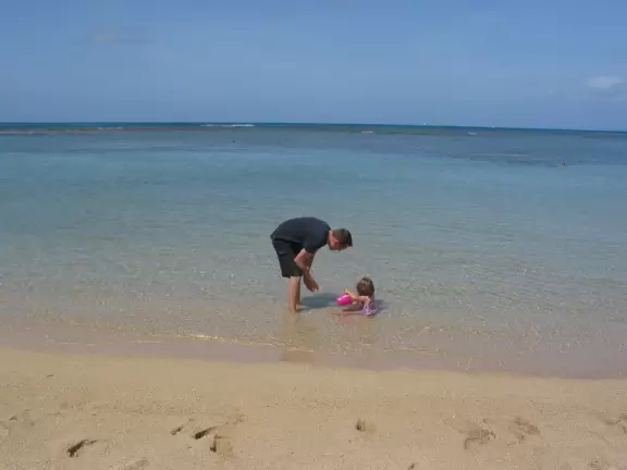 A father and baby girl in the calm waters close to shore. 