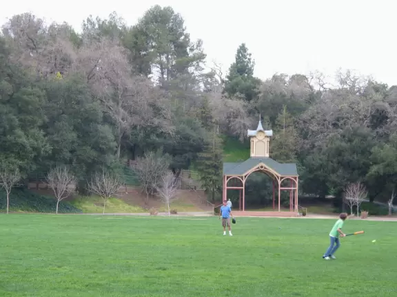 A father and son play ball at Oak Meadow Park, with the lovely hill covered in trees behind.