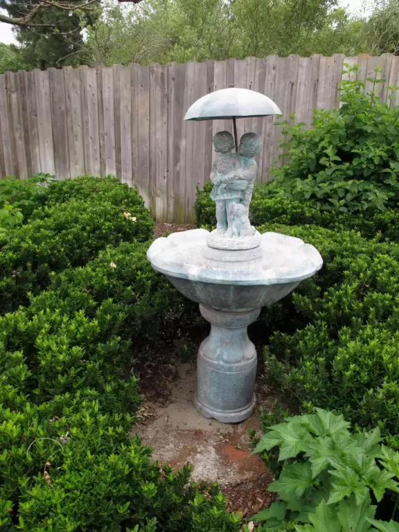 Birdbath sculpture of children under an umbrella.