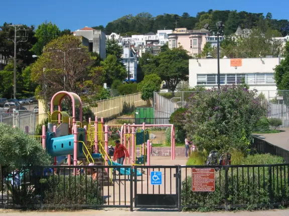Fenced playground at Duboce Park, with mountains in background.