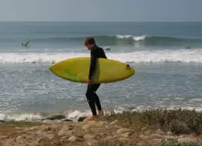 A surfer makes his way over the large pebbles to the water near the point. 