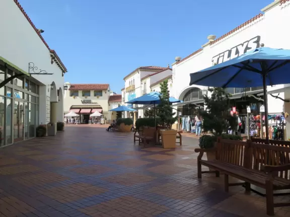 White Spanish-style buildings in an outlet mall, with views of hills from the parking lot.
