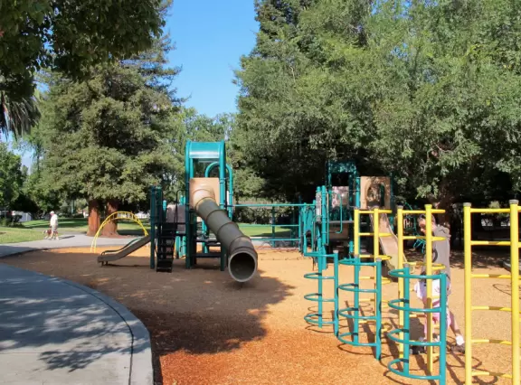 Large park with two colorful play areas and beautiful redwood trees.