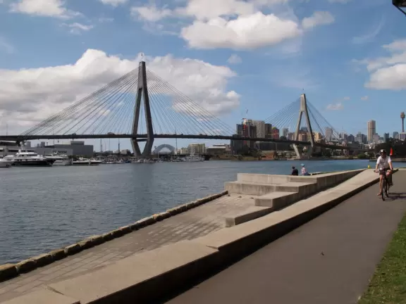 Gorgeous views of the city skyline and Anzac Bridge from a cement walking path alongside the water.