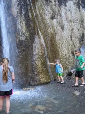A little girl puts her hand in the waterfall.