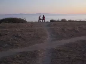 Friends sit on a bench over the sea at night.