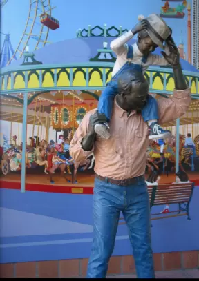 The statue and mural of a father with his son on his shoulders at a fair.
