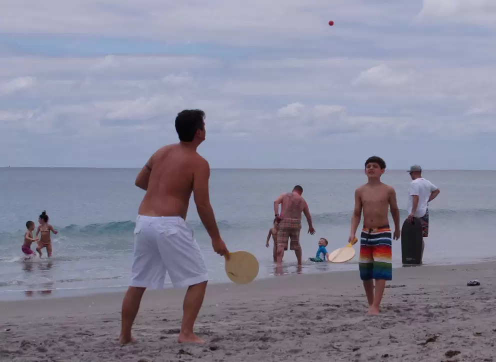 Father and son play paddle ball at the shoreline.