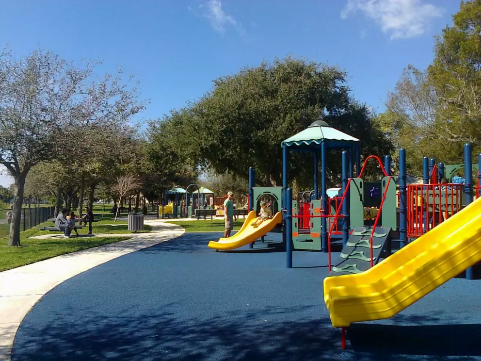 There are trees providing shade around the perimeter of the playground.