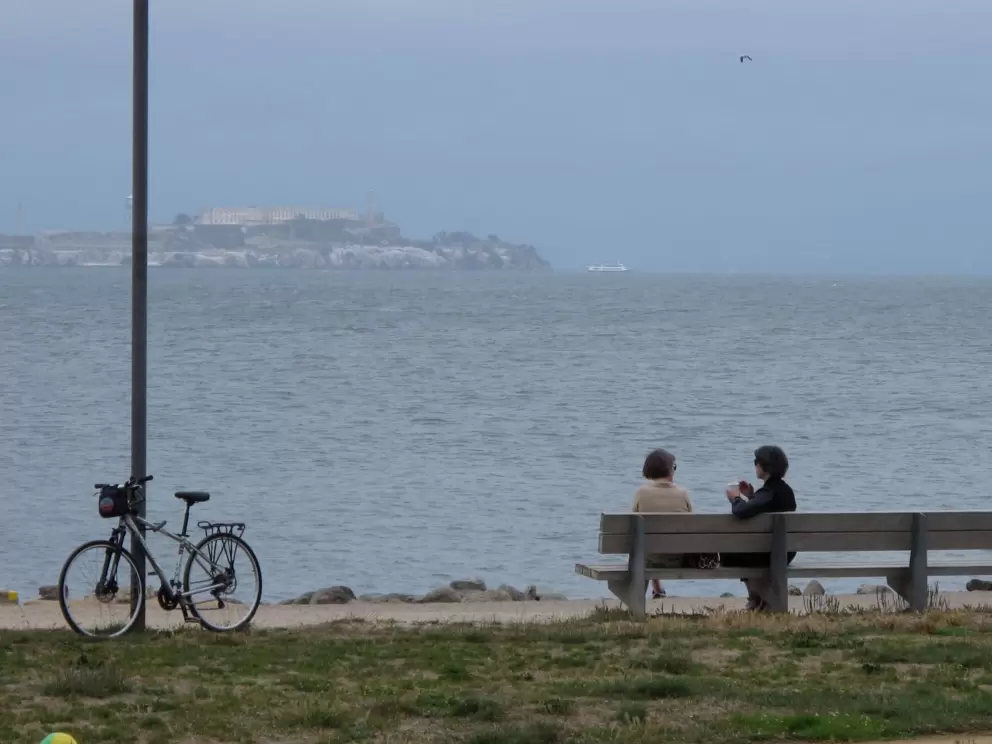 Women chat on a bench by the water.