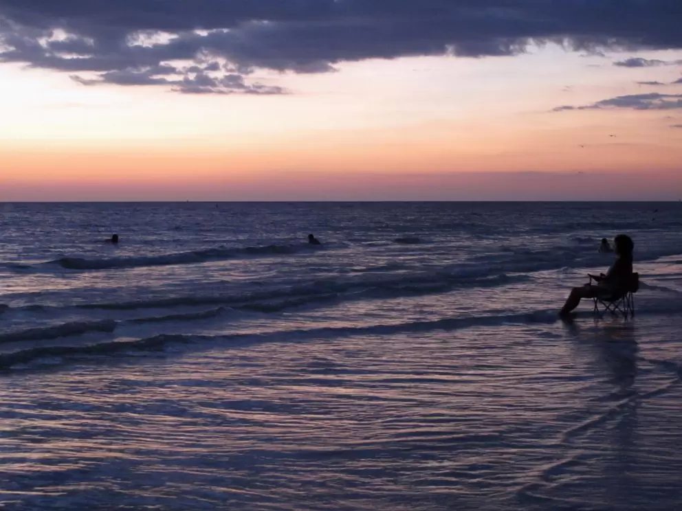 A lady sits in a beach chair in the water at shore!