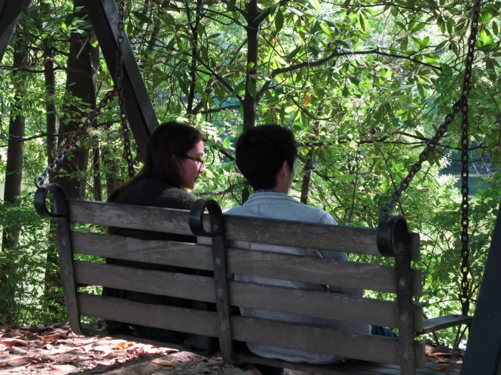 A couple chat on the swinging bench beside the lake.