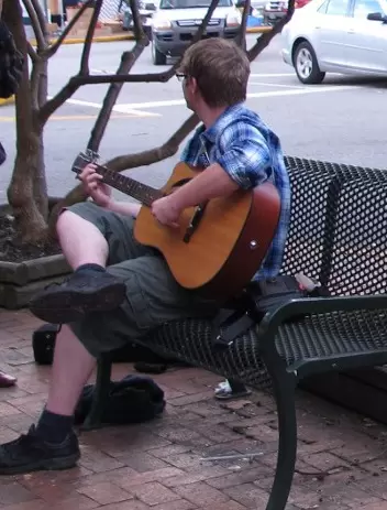 A student plays guitar as cars go by at the town square.