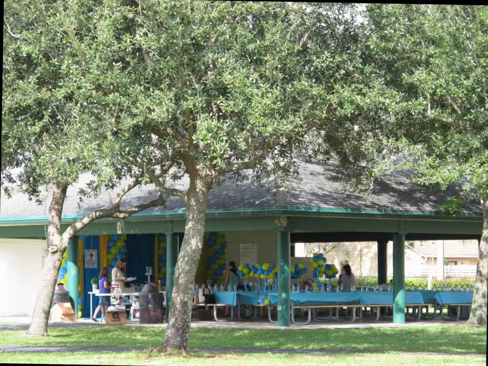 A party in a pavilion across the grass from the playground.