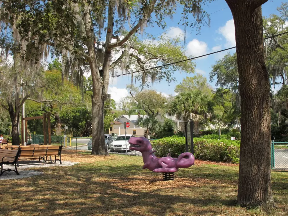 Purple dinosaur bouncy, picnic tables with chair backs, and trees for shade.