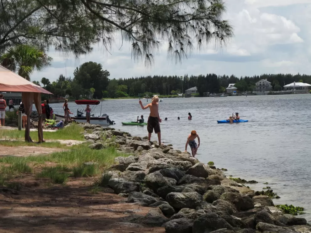 Two boys explore the rocks, while people kayak in the background.