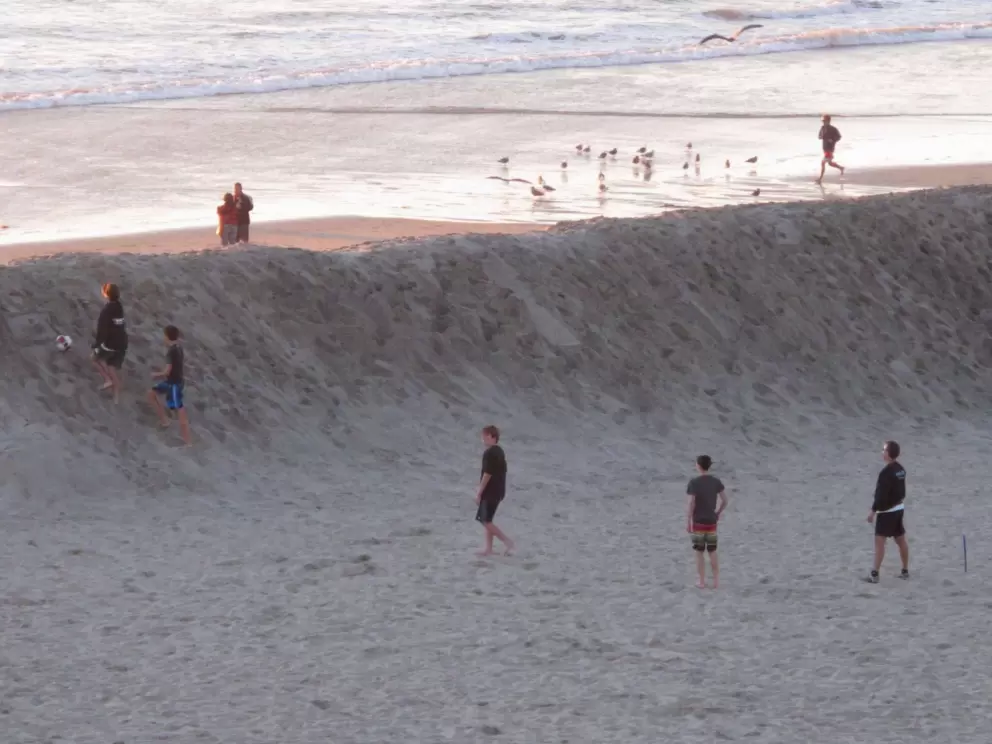 Guys playing soccer behind the wall of sand.