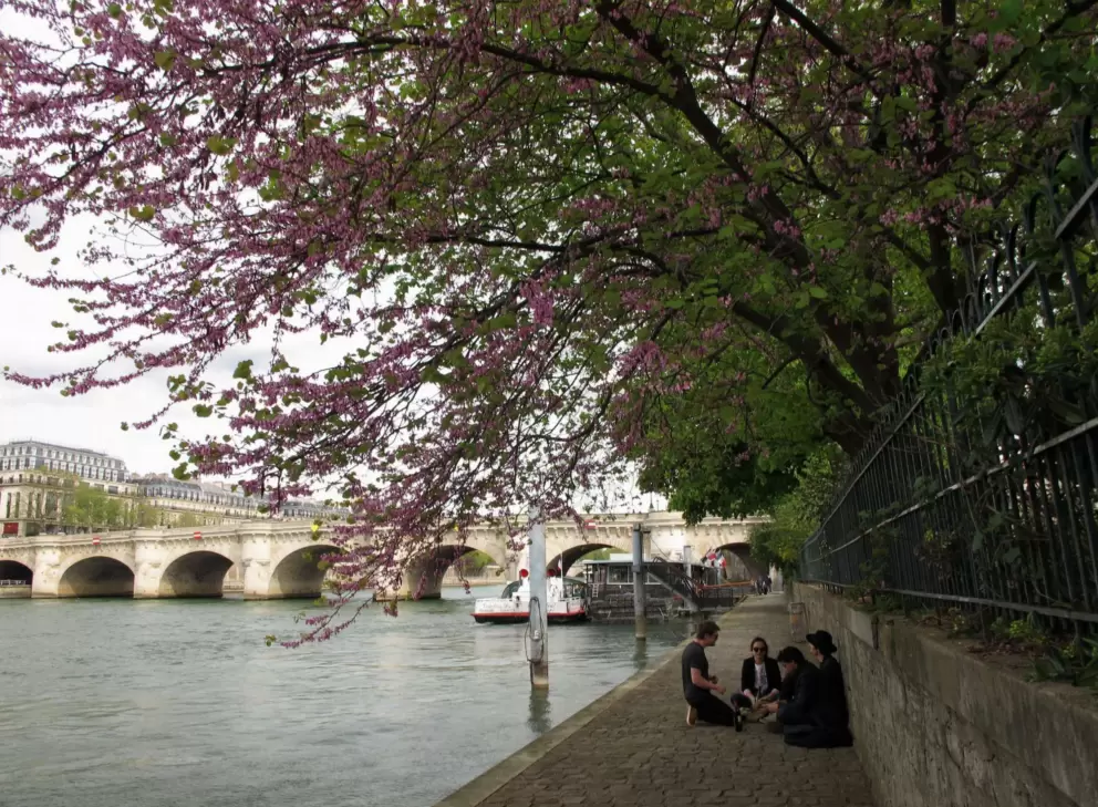 A group of young people hang out, with views of Pont Neuf behind them.
