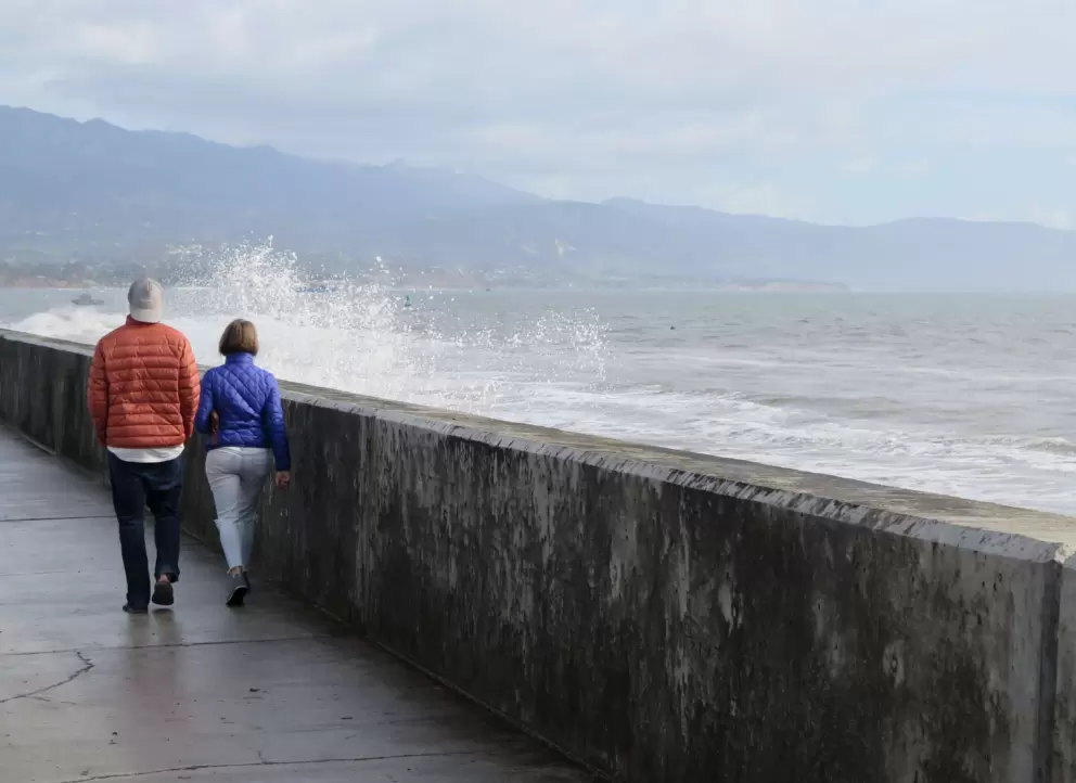 A couple strolls along as water sprays up.