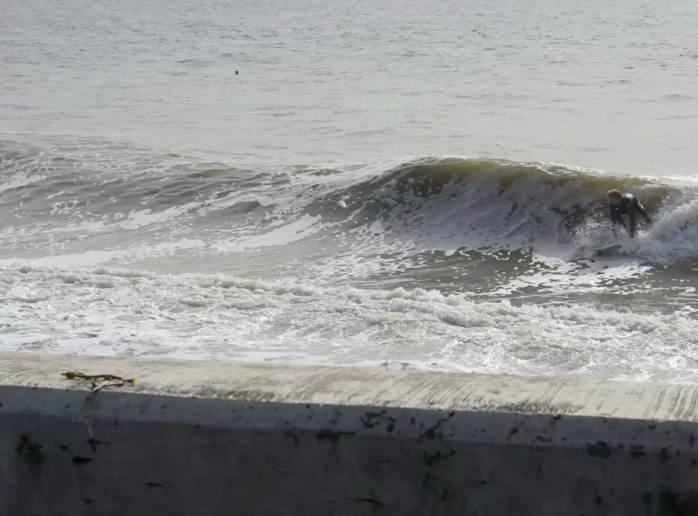 A surfer catches a wave by the seawall on a high surf day.