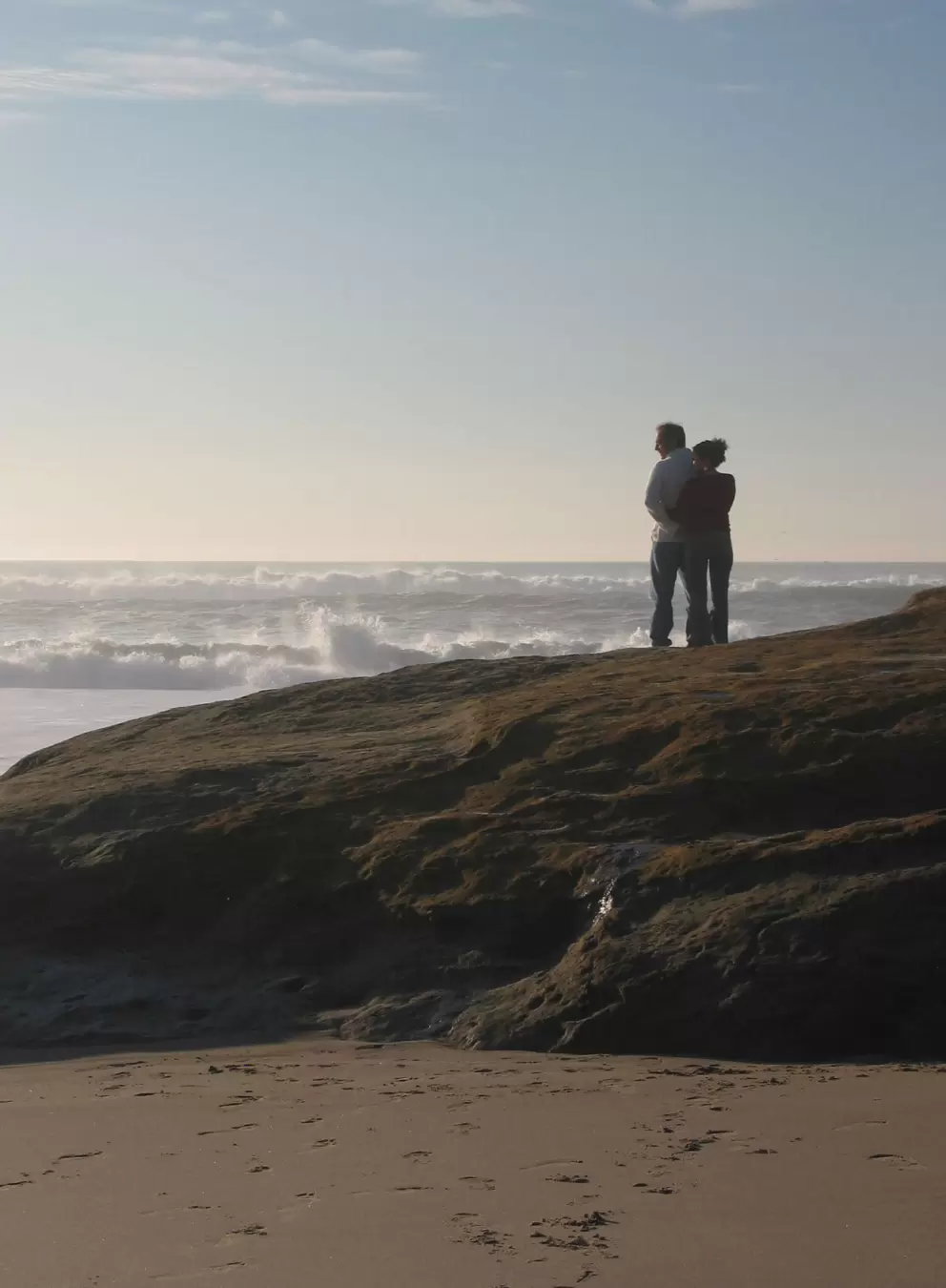 A loving couple stand and listen to the sea.