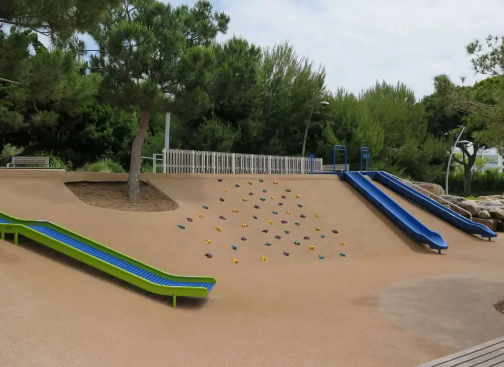 The playground with roller slide, two slides going down the hill, and rock climbing grips on the hill.
