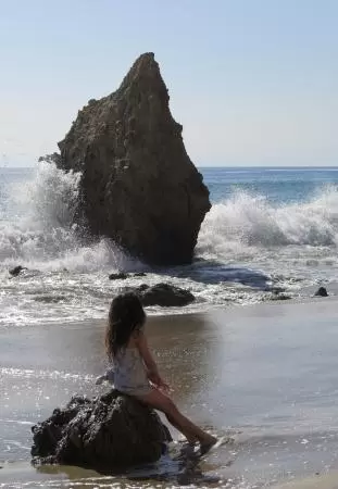 A little girl watches water crash on a rock.