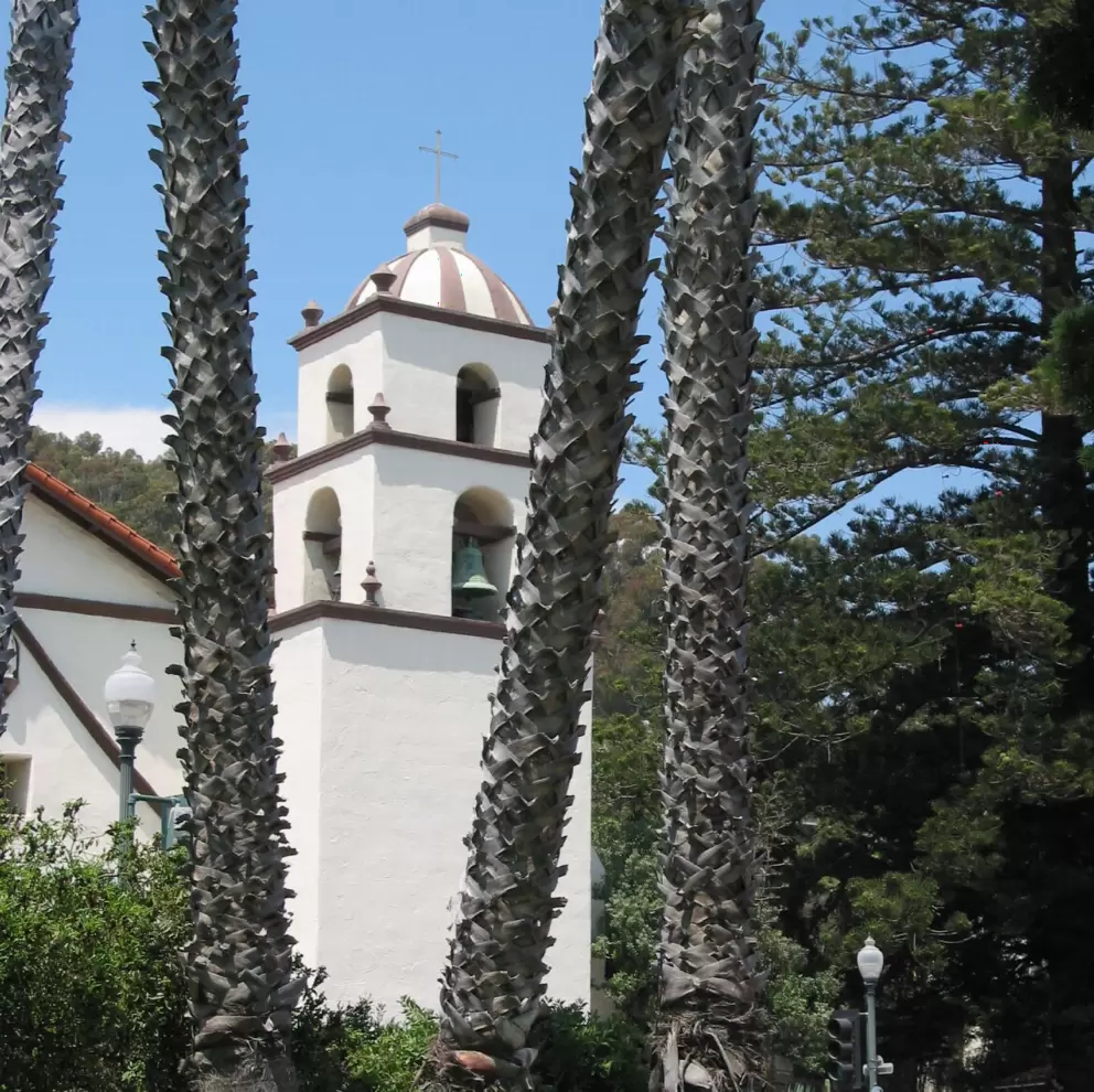 The mission is backed by mountains and surrounded by trees. 