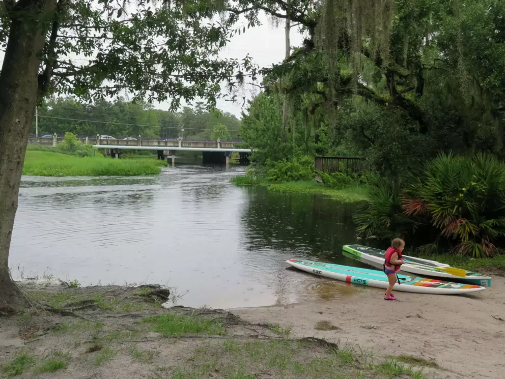 A little toddler in a life vest by kayaks.