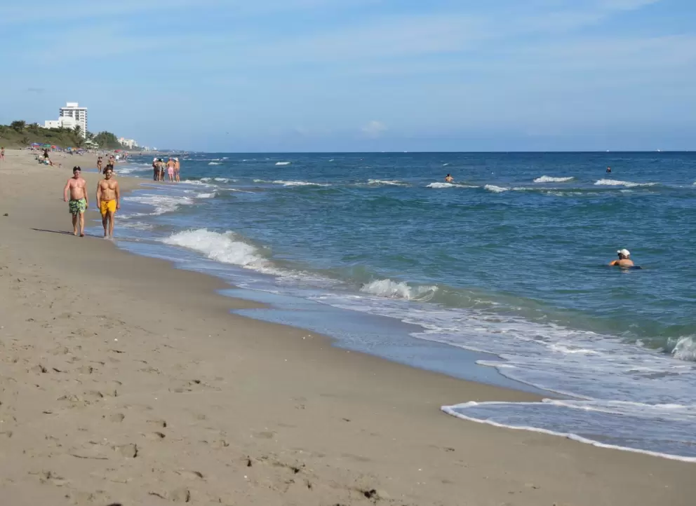 Two men walk along the shore as a lady swims.