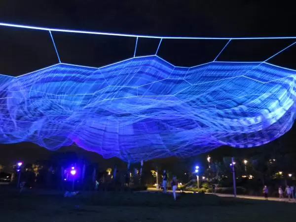 Web in the sky, lit with lasers at night, by the playground on the pier.