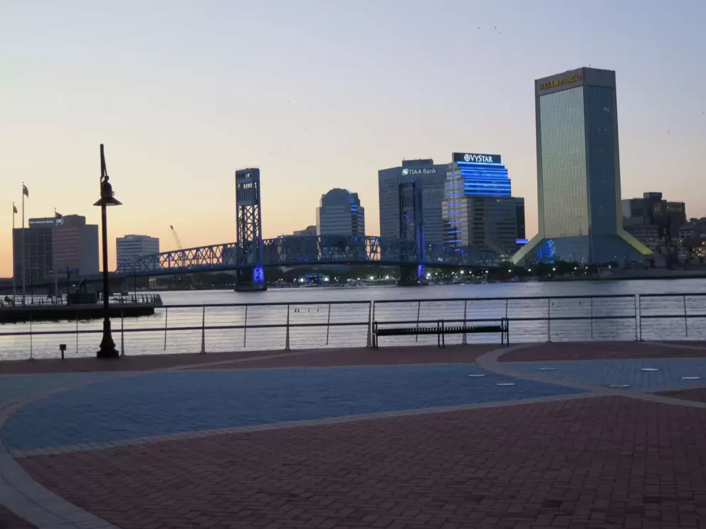 The blue and green buildings, and Main Street Bridge, as seen from a wide open area along the riverwalk.