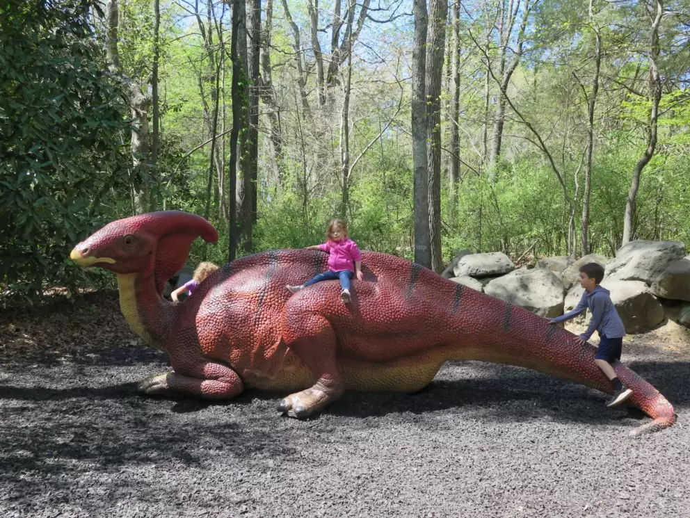 A toddler sits on a dinosaur.