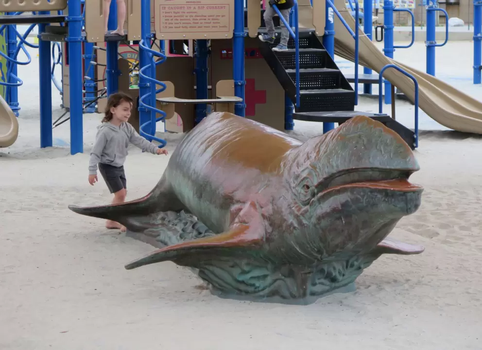 A girl runs to the whale sculpture. 