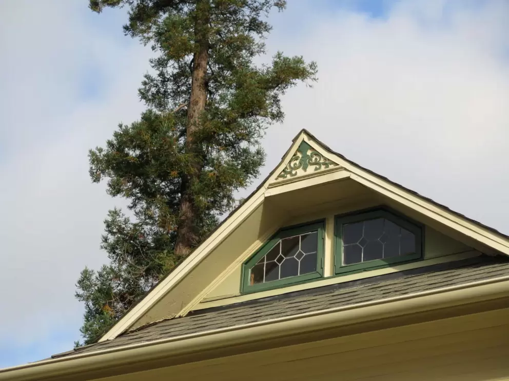 Pointy gable with stained glass windows, and a pine tree behind. 