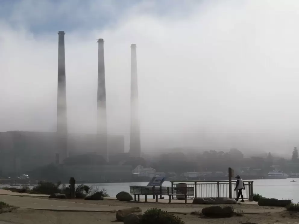 The smoke stacks in fog and someone walking the path. 