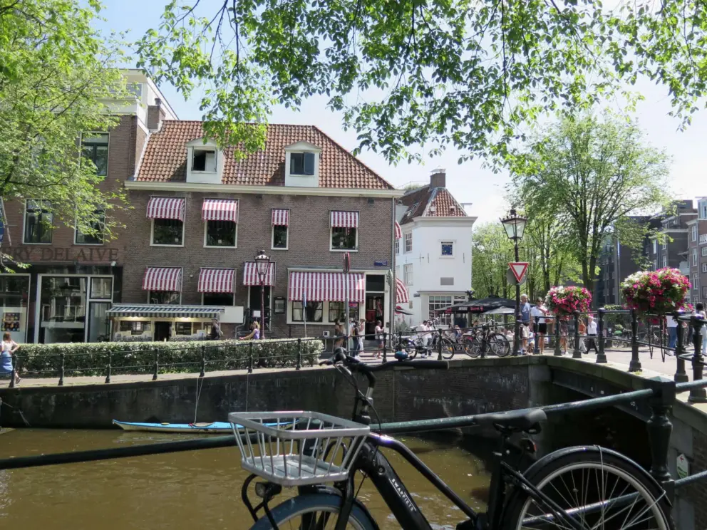 Bike, bridge over a canal, and building with striped awnings. 