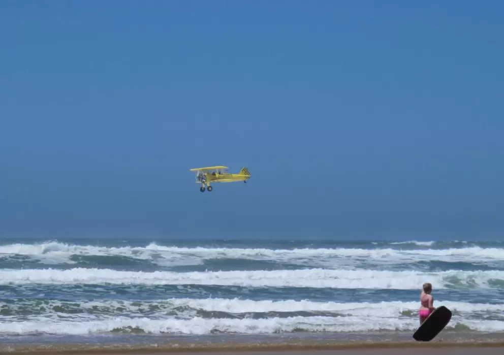 Child with bodyboard, and yellow biplane from Oceano zooming by doing tricks.