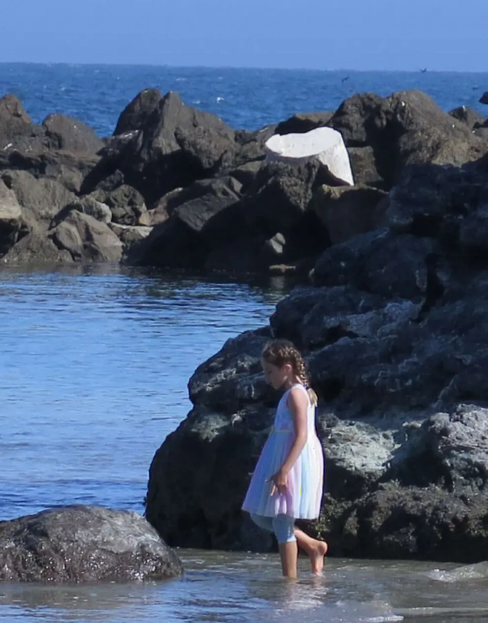 A girl by the rocks on the far end of the beach. 

