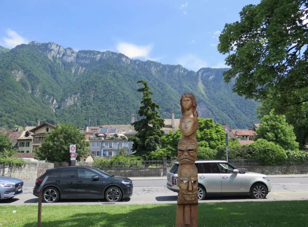Wooden statue, and high mountains behind, at the waterfront. 