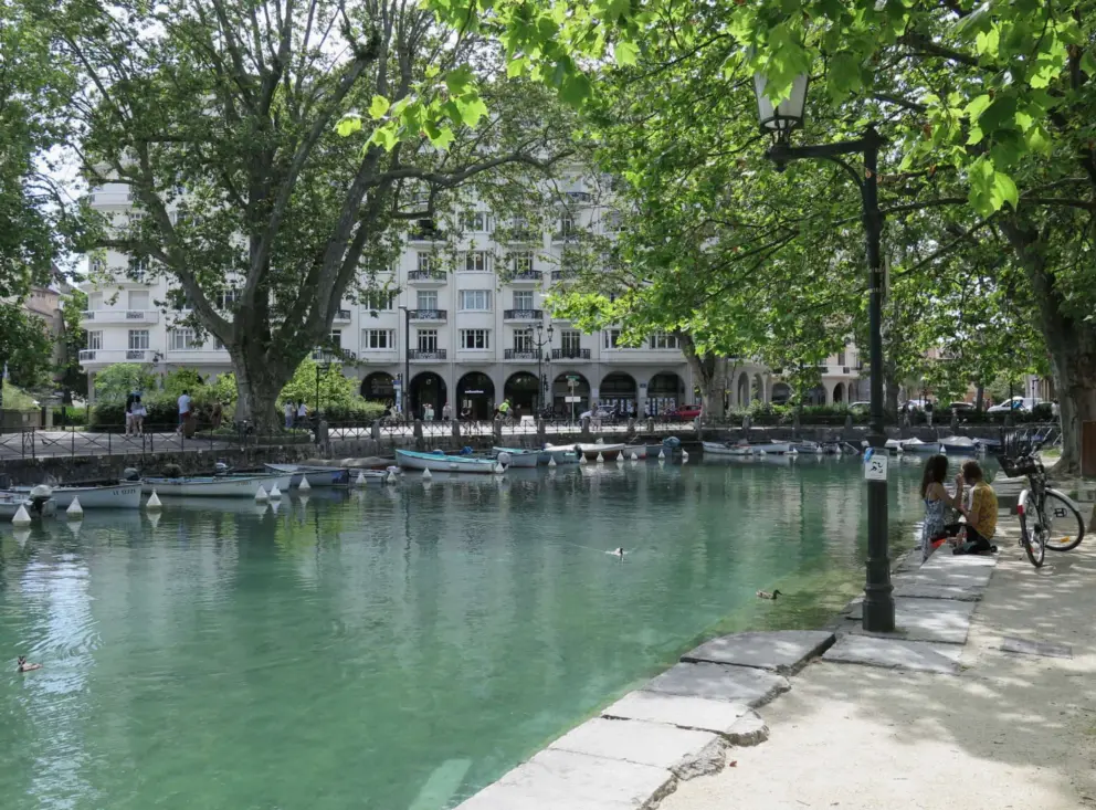 A couple sits in the shade by the canal. 