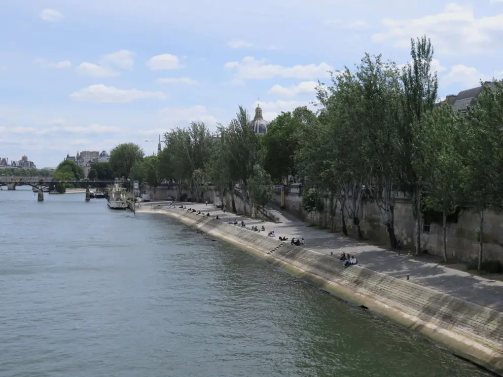 The promenade on the left bank of the Seine River, with people sitting on the bank. 