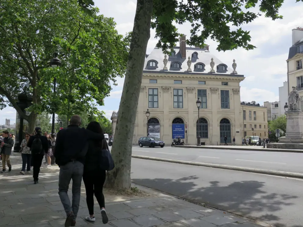 A couple walks by the booksellers, with Academie des Beaux-Arts in the distance. 
