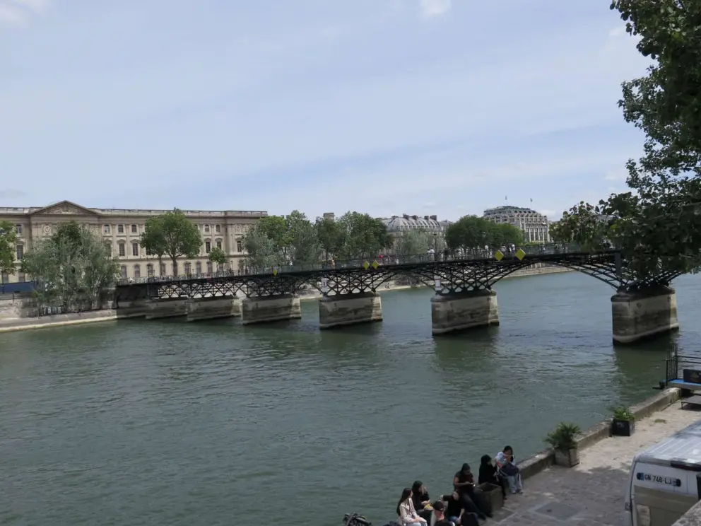 Looking down at Pont des Arts and people sitting on the banks of the Seine beside it. 