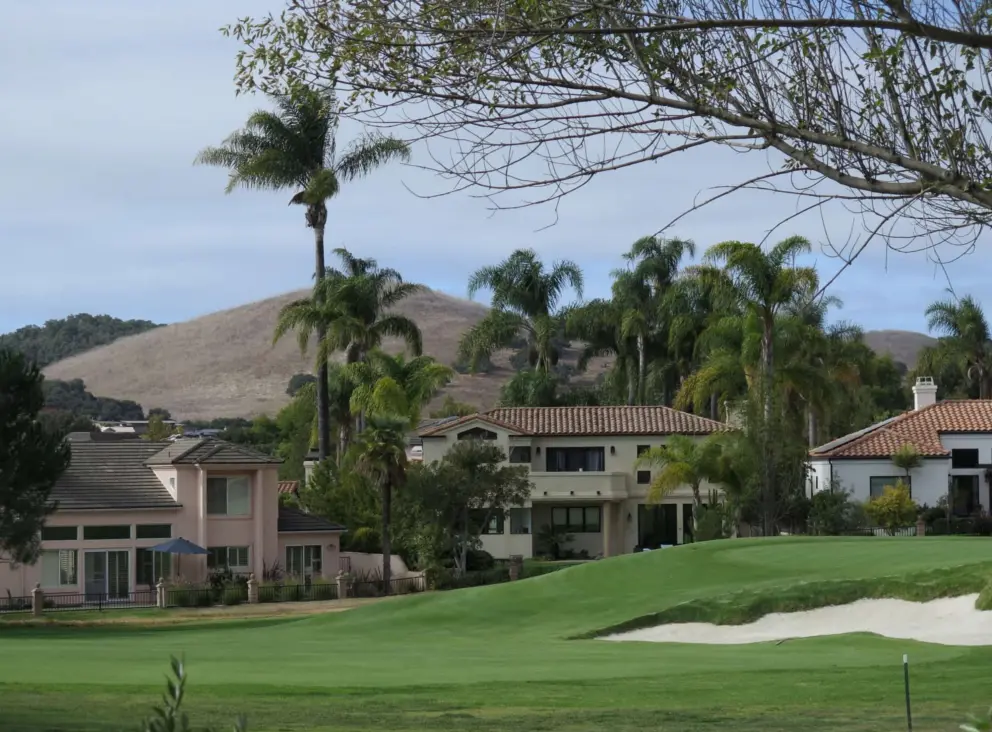 Golf course and palm trees, with hills behind. 