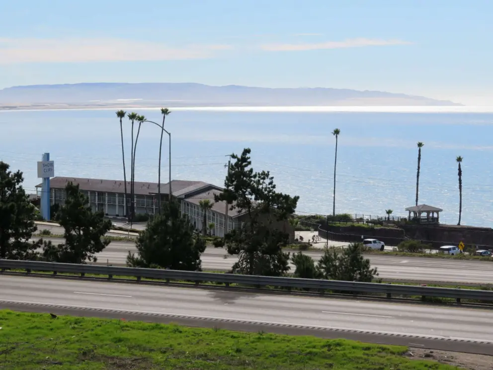 View of Shore Cliff Lodge, its gazebo, and the sparkling sea, from the parking lot at Pismo Preserve. 