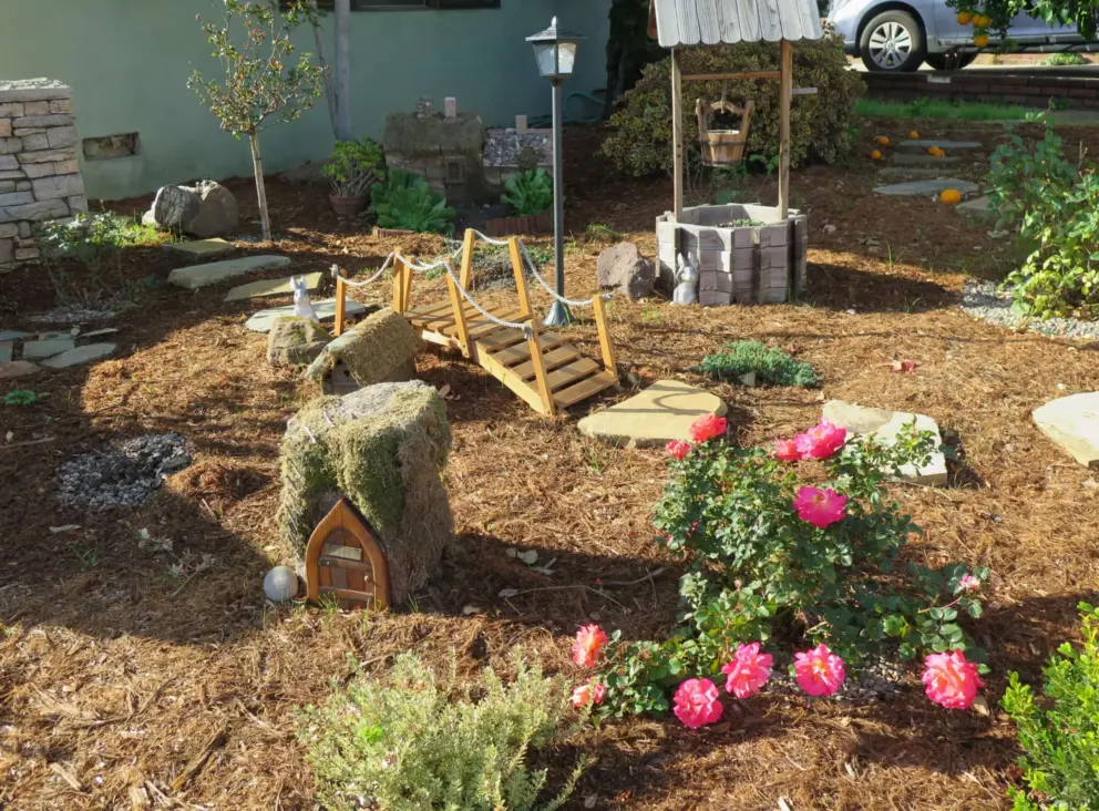 A little fairy garden with bridge, water well, stepping stones, and structure with fairy door.