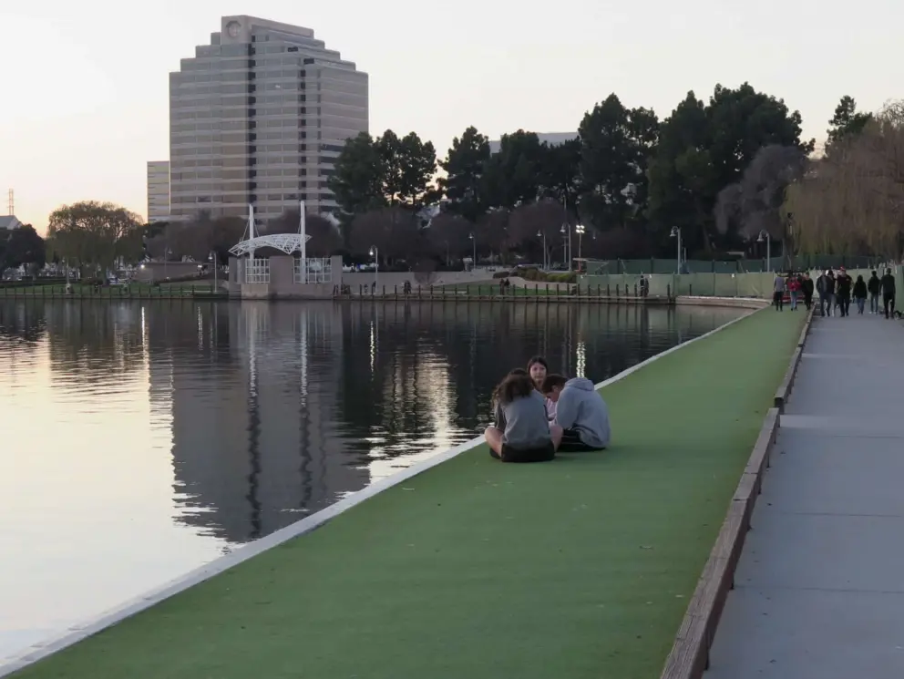 The Metro Tower reflected in the lagoon, and teens sitting by the water. Foster City is a very safe spot.