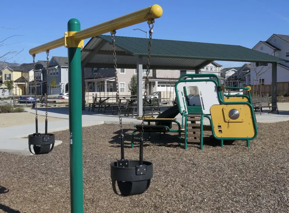 Baby swings and toddler playground, with picnic pavilion behind. 